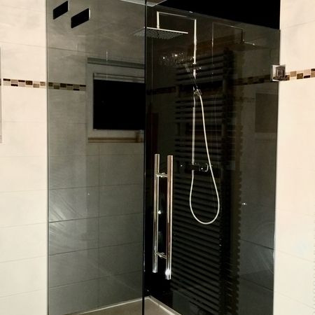 Glasdusche auf grauem Untergrund mit schwarzer Fliesenwand