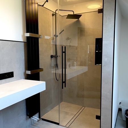 Glasdusche mit beigen Fliesen und schwarzen Rahmenelementen