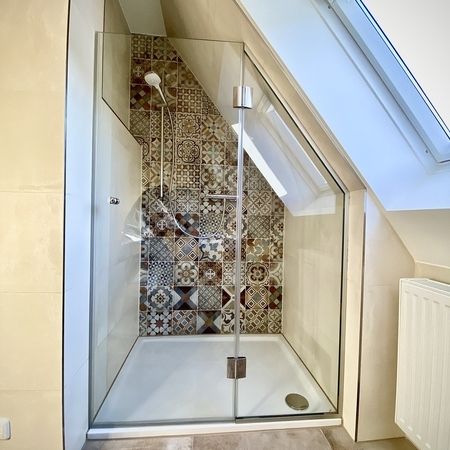 Glasdusche unter einer Dachschräge mit dekorativen Fliesen