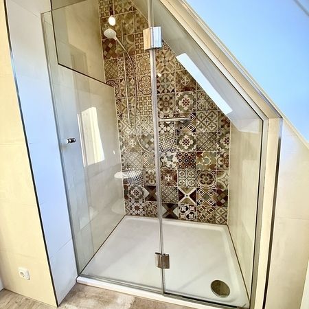 Glasdusche unter einer Dachschräge mit dekorativen Fliesen