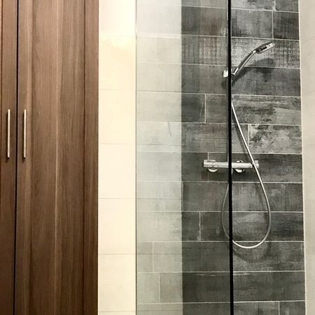 Glasdusche rechts mit grauen Fliesen, dunkelbrauner Schrank links