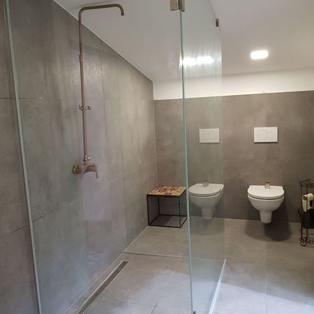 Grau gefliestes Bad mit Glasdusche im Vordergrund und Toilette im Hintergrund