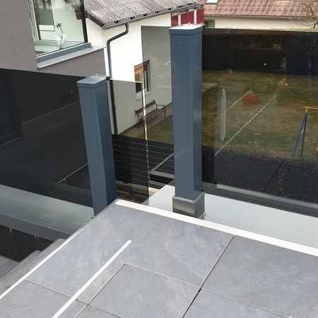 Grauer Fliesenbalkon mit dunklem Glasgeländer