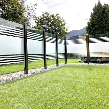 Gestreiftes Glasgeländer einer Steinterrasse, Ansicht von innerer Grasfläche