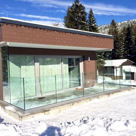 Terrassen-Glasgeländer vor Backsteinhaus, umgeben von Schnee und Nadelbäumen