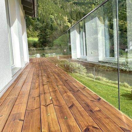 Rechte Innenansicht eines Holzterassen-Geländers mit Blick auf eine grüne, sonnige Landschaft