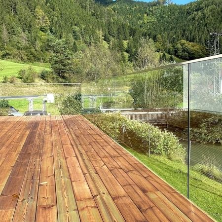 Innenansicht eines Holzterassen-Geländers mit Blick auf eine grüne, sonnige Landschaft