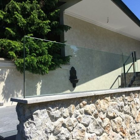 Glasgeländer auf einer Steinmauer vor einem Haus mit Baum
