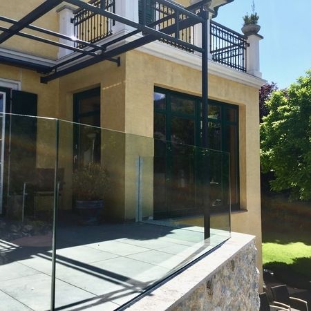 Gläsernes Terrassengeländer vor einem gelben Haus mit Garten