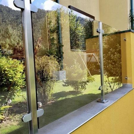 Glasgeländer auf gelber Mauer vor grüner Wiese mit Büschen