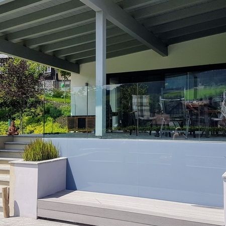 Eingangsbereich eines hellen Hauses mit Überdachung, Treppe links und Glasgeländer rechts