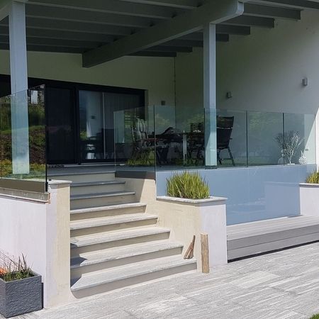 Eingangsbereich eines hellen Hauses mit Überdachung, Treppe mittig mit beidseitigem Glasgeländer